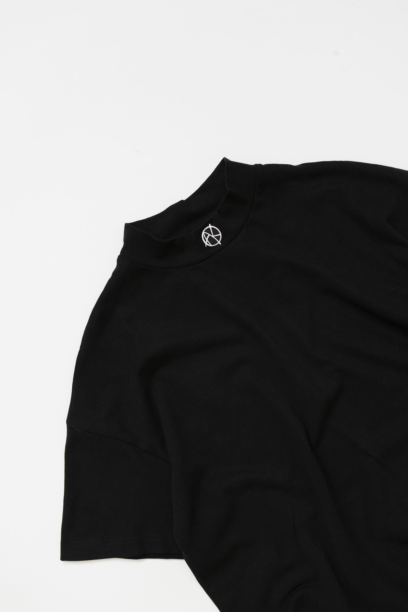CLOSE UP VIEW OF AK LOGO EMBROIDERY ON MOCKNECK TEE IN FLAT LAY